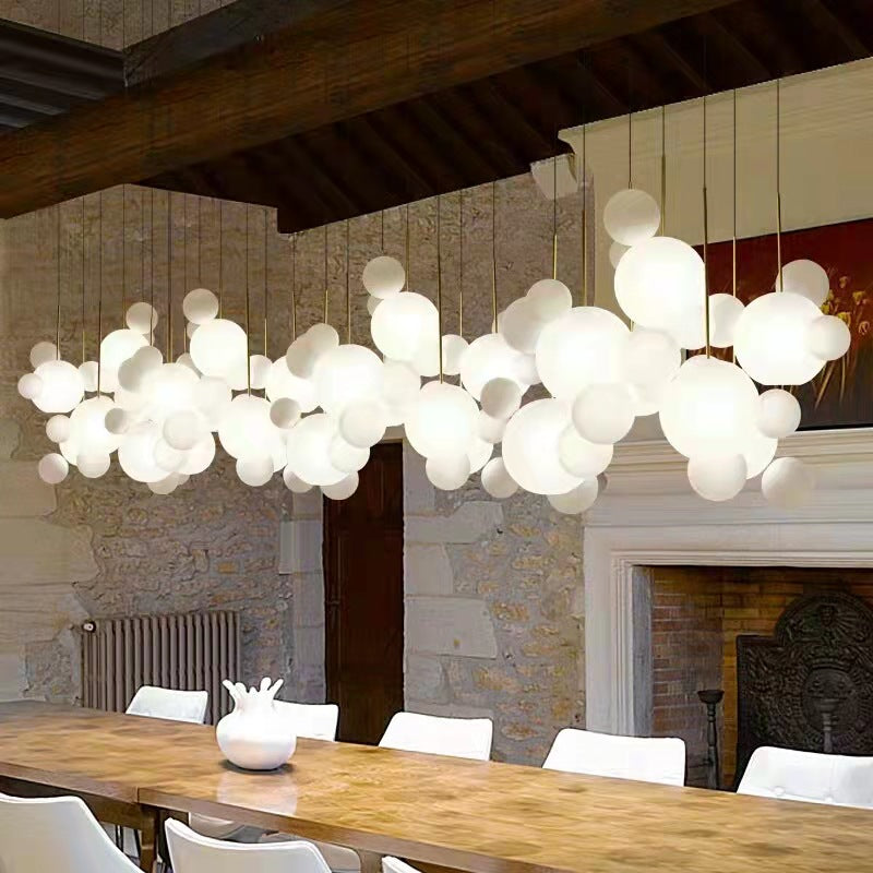 The Ethereal Cloud frosted glass bubble chandelier making a grand statement over a modern dining table, illuminated, showcasing its full cluster form.