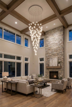Modern living room with high ceiling, chandelier, stone fireplace, and large windows.
