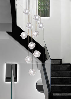 The large Aria stone glass chandelier with a chrome frame hanging as a centerpiece on the staircase setting.